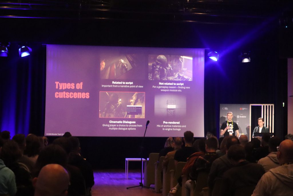 Audience in a dark auditorium watching a projector screen titled 'Types of cutscenes' with two presenters on stage under blue lighting.