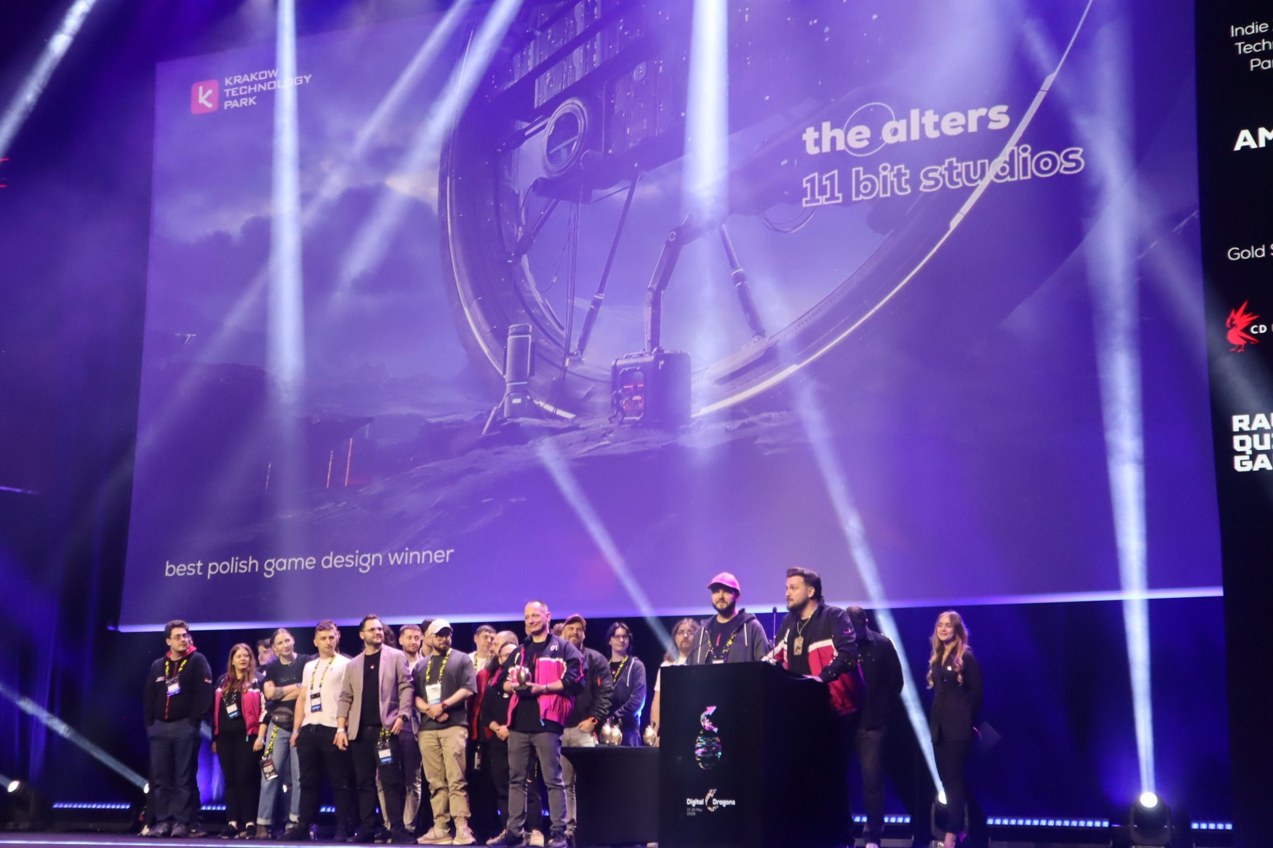 Group of people posing on a stage at a tech ceremony, with a purple backdrop reading 'the alters' and '11 bit studios'.