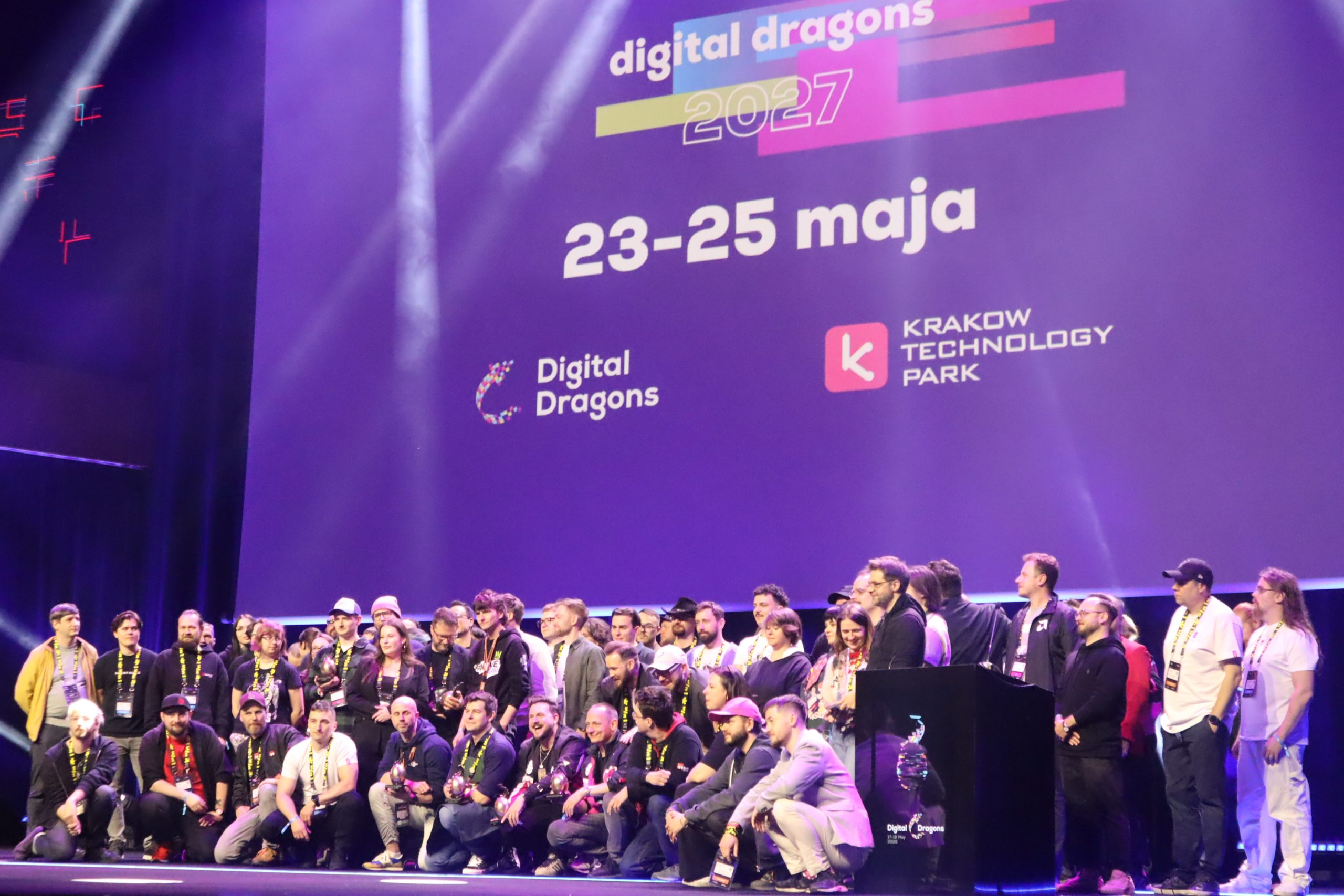 Group of people on a stage in front of a purple backdrop reading 'digital dragons 2027' with dates 23-25 maja and logos, at a tech event.