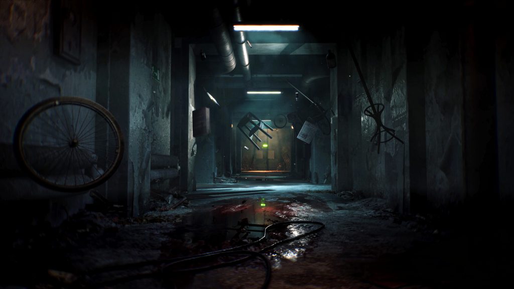 Dark, abandoned basement corridor with a broken bicycle wheel against the wall and scattered debris on a wet floor. A green exit sign glows in the distance under harsh fluorescent lighting.