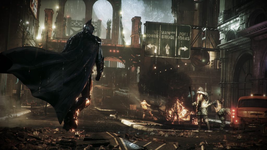 Batman stands on a rain-soaked, ruined city street, cape billowing, facing a crowd of zombies amid fires and debris at night.