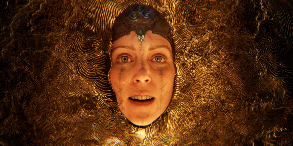 Close-up of a woman's face with facial markings and a small jewel, surrounded by swirling gold texture.